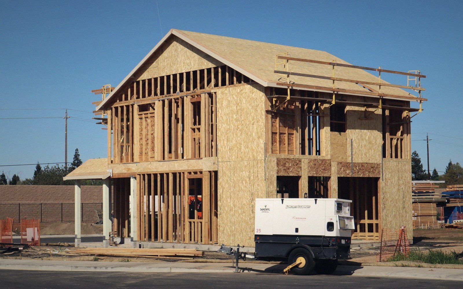 A two-story house under construction with plywood sheathing and a towable generator parked outside