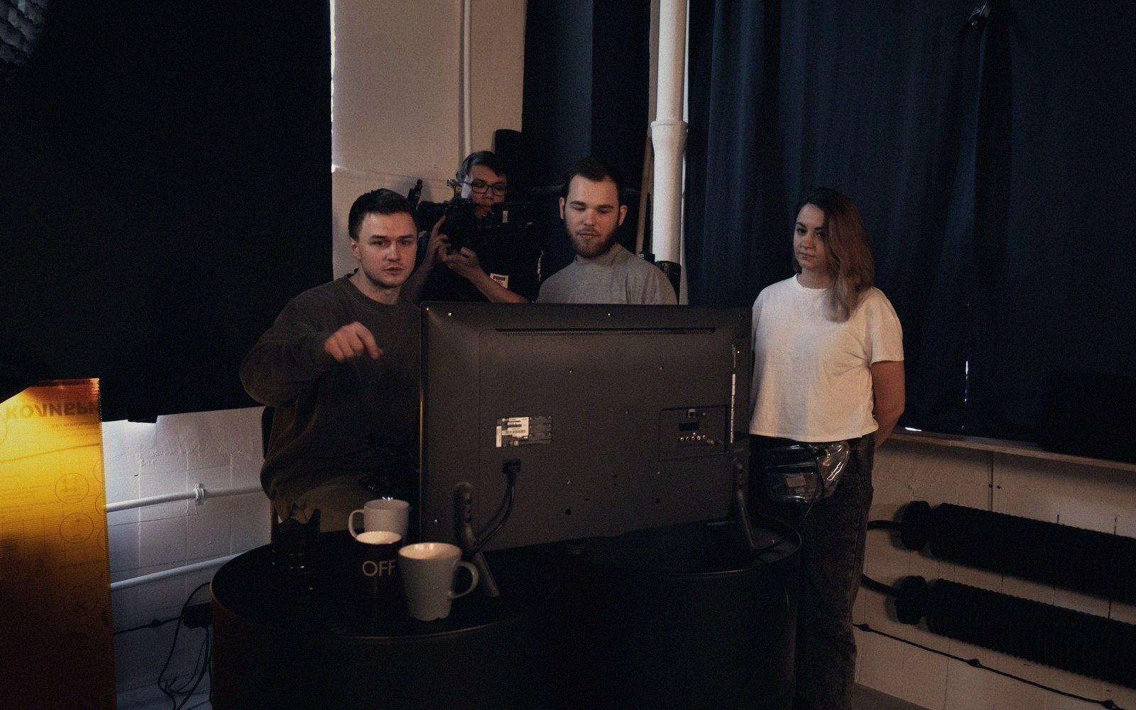 Crew members gather behind a monitor on a film set with dark curtains
